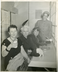 Four well dressed women sit at a bench inside a prison cell.